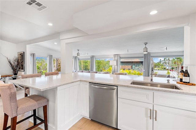 kitchen with sink, dishwasher, white cabinetry, a kitchen breakfast bar, and light stone counters