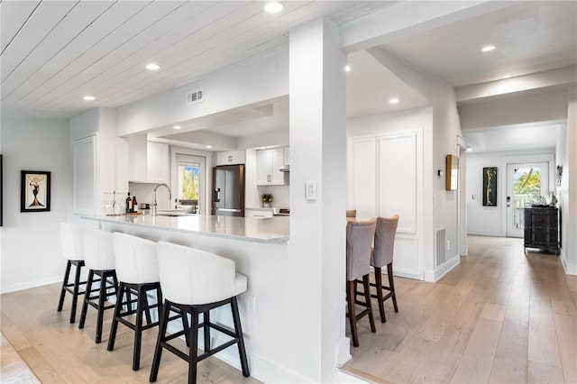 kitchen with a breakfast bar area, light hardwood / wood-style floors, white cabinets, stainless steel fridge with ice dispenser, and kitchen peninsula