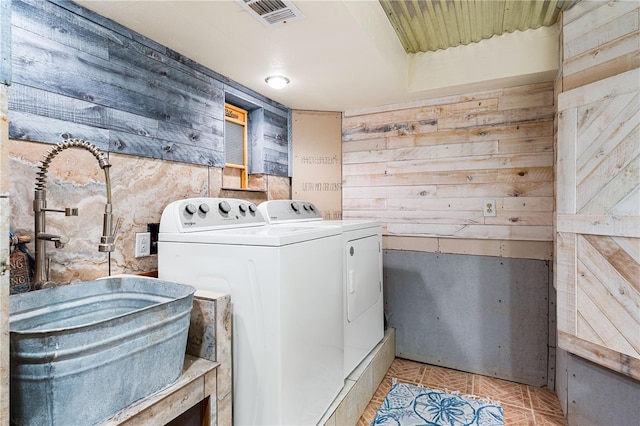 clothes washing area with light tile patterned flooring, washing machine and clothes dryer, and wood walls