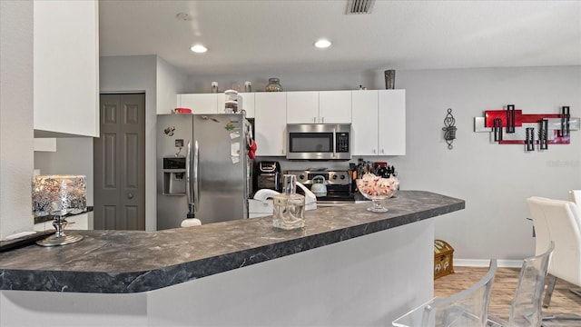 kitchen featuring kitchen peninsula, white cabinetry, a breakfast bar, and appliances with stainless steel finishes