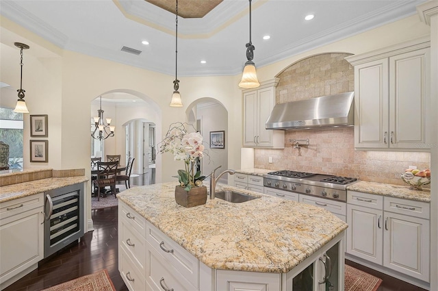 kitchen featuring a kitchen island with sink, pendant lighting, beverage cooler, and range hood