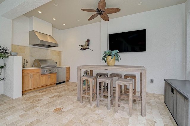 kitchen with sink, backsplash, wall chimney range hood, ceiling fan, and light brown cabinets