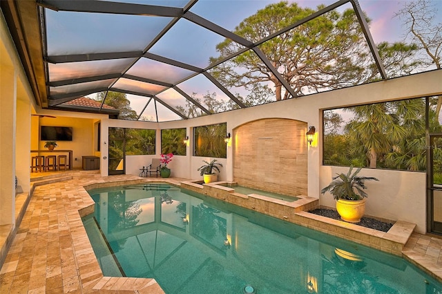 pool at dusk featuring a hot tub, a patio, a lanai, and an outdoor bar