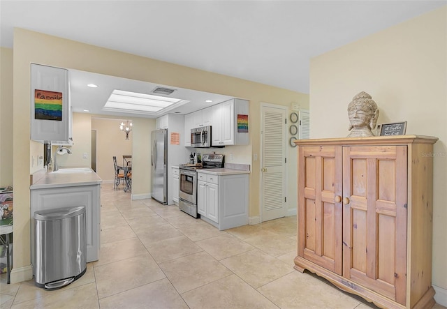 kitchen with light tile patterned floors, sink, white cabinetry, stainless steel appliances, and a notable chandelier