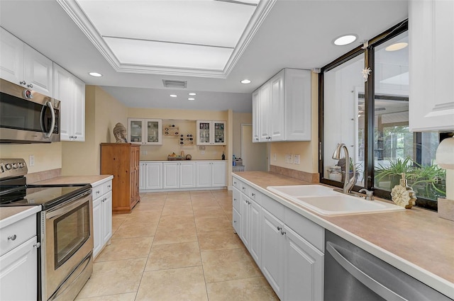 kitchen with light tile patterned flooring, sink, ornamental molding, appliances with stainless steel finishes, and white cabinets