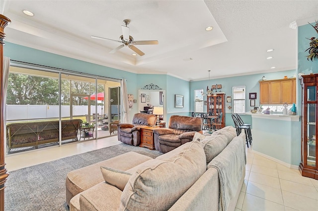 tiled living room featuring a raised ceiling, ornamental molding, a textured ceiling, and ceiling fan