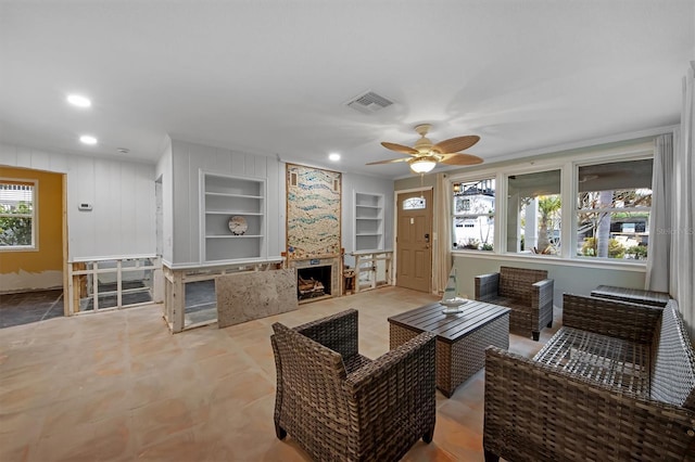 living room featuring a fireplace, built in features, and ceiling fan