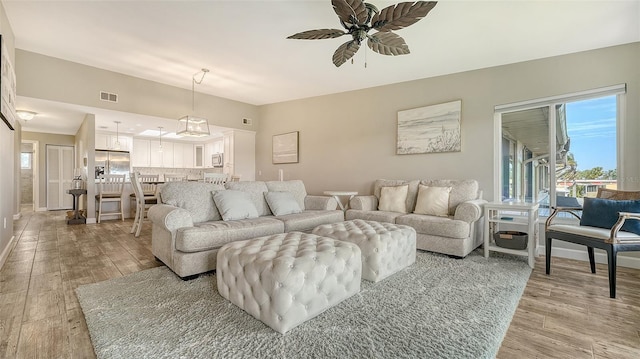 living room featuring baseboards, light wood-style flooring, visible vents, and a ceiling fan