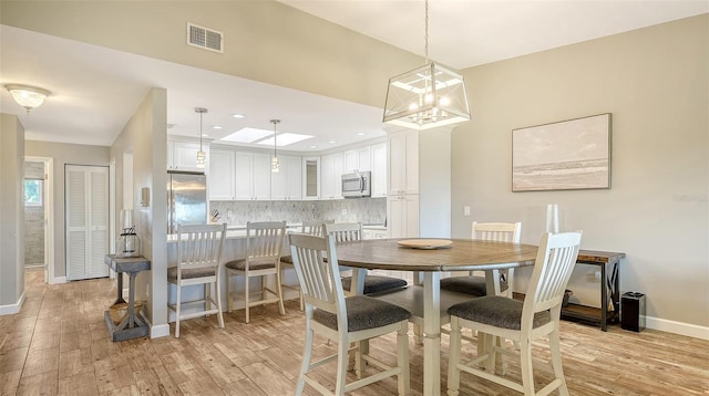 dining area featuring a chandelier, light wood-type flooring, visible vents, and baseboards