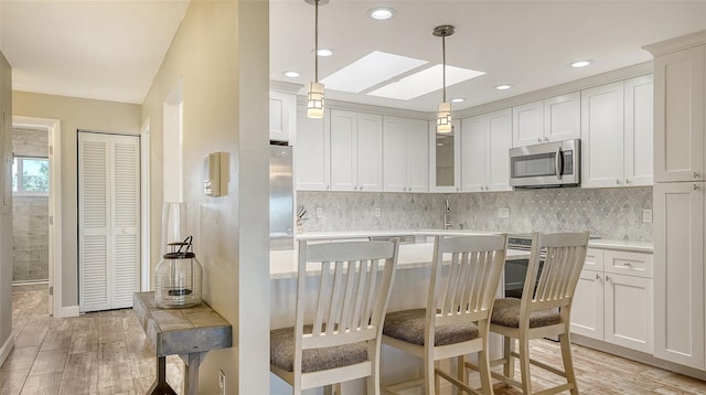 kitchen featuring light countertops, stainless steel microwave, decorative light fixtures, and white cabinetry