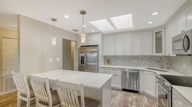 kitchen with stainless steel appliances, glass insert cabinets, a sink, and white cabinetry