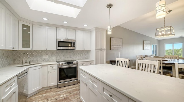 kitchen featuring glass insert cabinets, appliances with stainless steel finishes, white cabinets, and decorative light fixtures