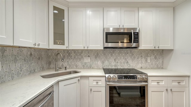 kitchen featuring glass insert cabinets, light stone counters, stainless steel appliances, white cabinetry, and a sink