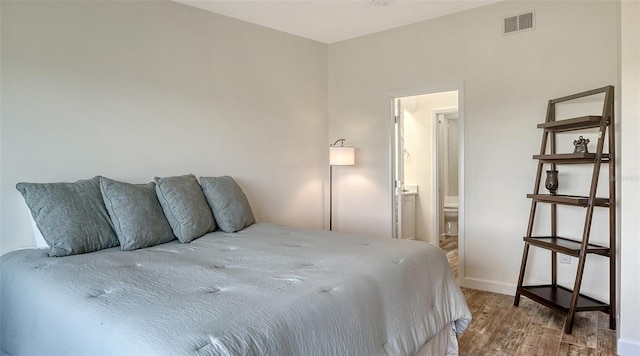 bedroom with ensuite bath, baseboards, visible vents, and wood finished floors