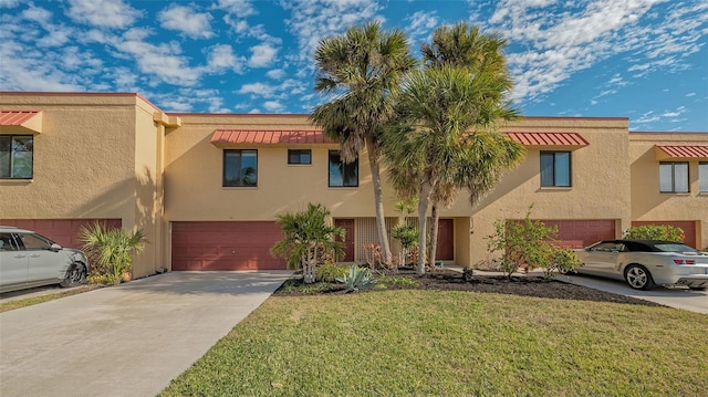 multi unit property with a garage, driveway, a front yard, and stucco siding