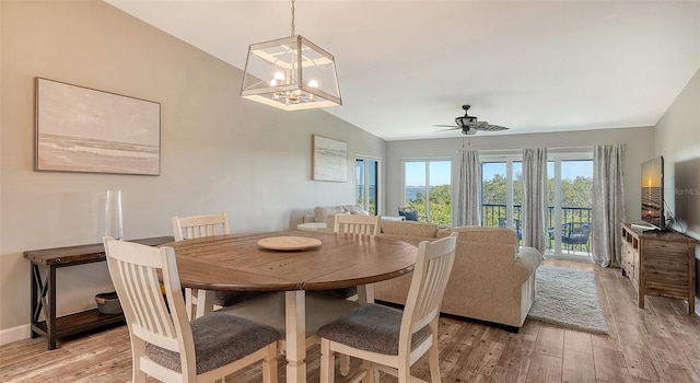 dining space featuring baseboards, vaulted ceiling, light wood finished floors, and ceiling fan with notable chandelier