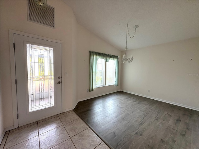 entryway featuring baseboards, visible vents, lofted ceiling, wood finished floors, and a chandelier