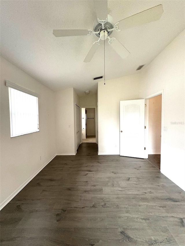 empty room with dark wood-style flooring, visible vents, vaulted ceiling, a textured ceiling, and ceiling fan