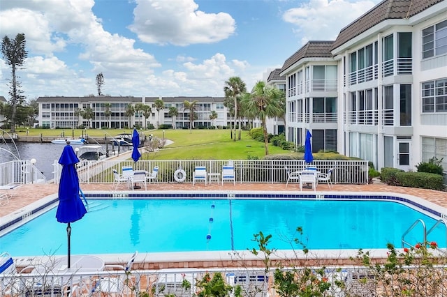 community pool with a lawn, a water view, and fence