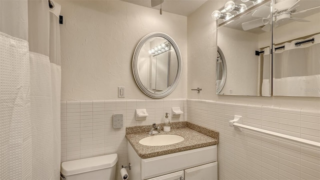 bathroom featuring tile walls, toilet, a ceiling fan, wainscoting, and vanity