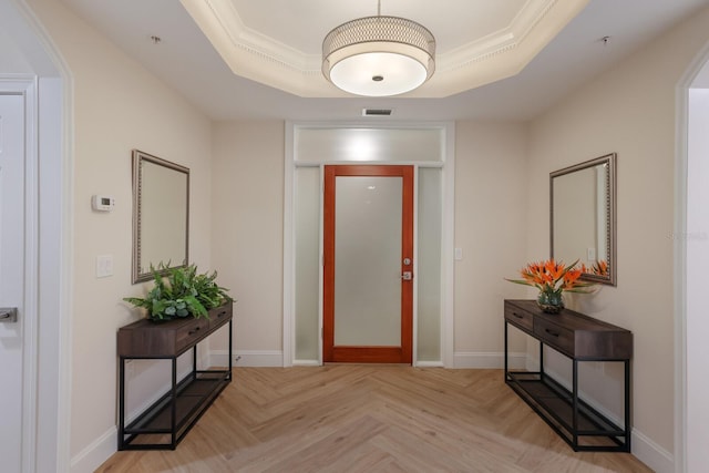 interior space with a tray ceiling, ornamental molding, and light parquet flooring