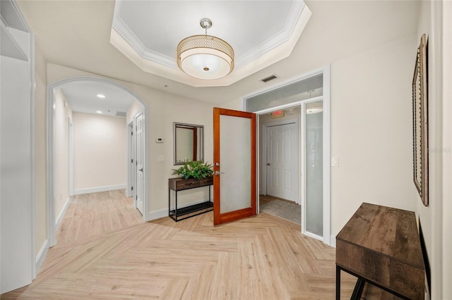 hallway featuring ornamental molding, a raised ceiling, and light parquet floors