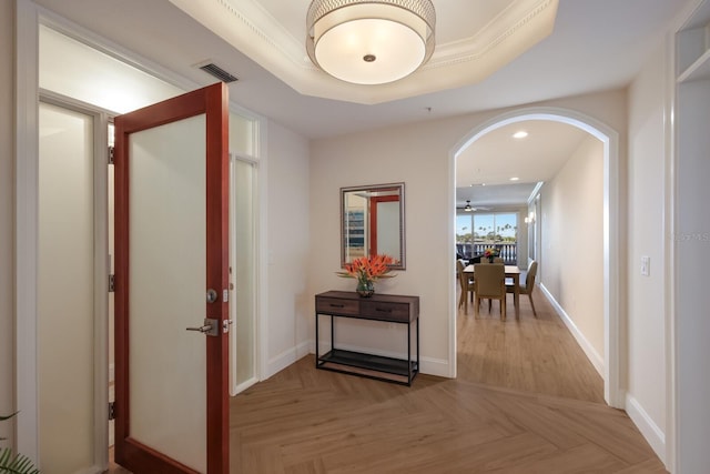 hall with light parquet floors, a raised ceiling, and ornamental molding