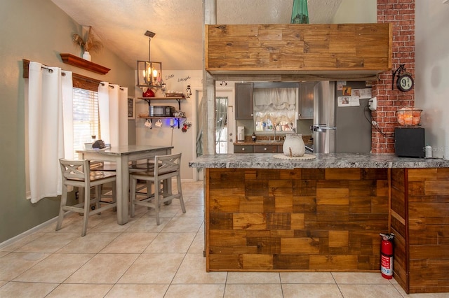 kitchen with kitchen peninsula, pendant lighting, stainless steel fridge, light tile patterned floors, and lofted ceiling