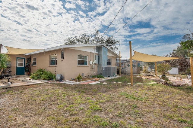 rear view of property featuring central AC unit and a lawn