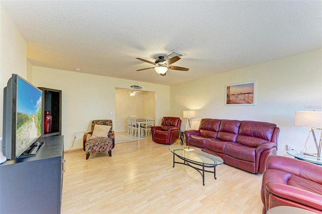 living room featuring light wood-type flooring, a textured ceiling, and ceiling fan