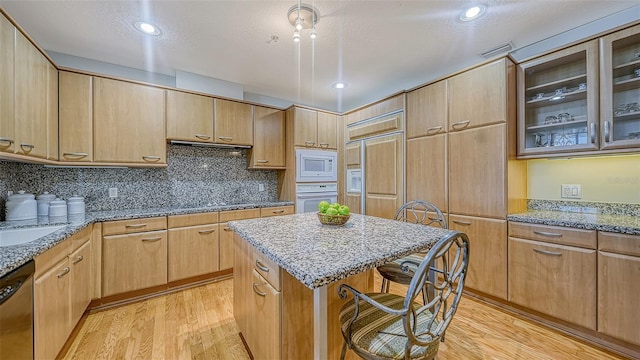 kitchen with built in microwave, oven, stainless steel dishwasher, a kitchen island, and light stone countertops