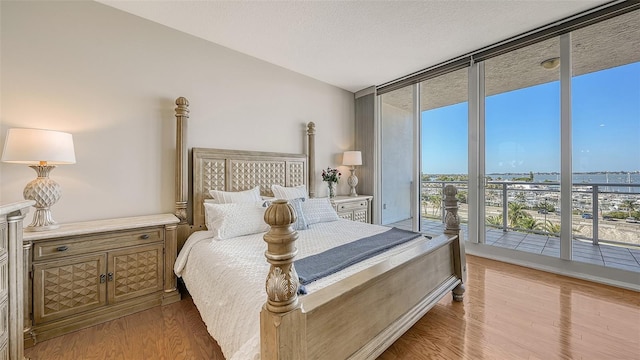 bedroom with access to outside, light hardwood / wood-style floors, floor to ceiling windows, and a textured ceiling