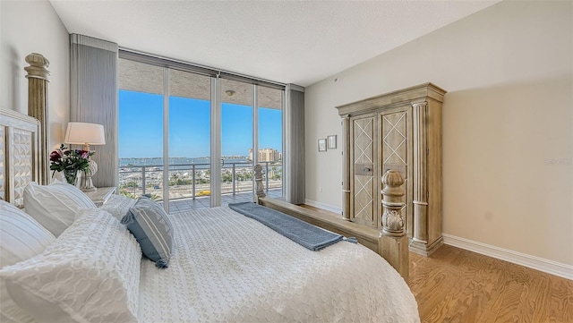 bedroom with a wall of windows, access to exterior, multiple windows, and light wood-type flooring