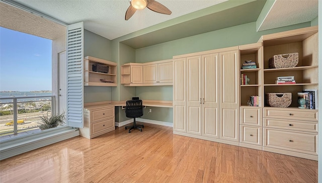 office space featuring light wood-type flooring, built in desk, a textured ceiling, and ceiling fan