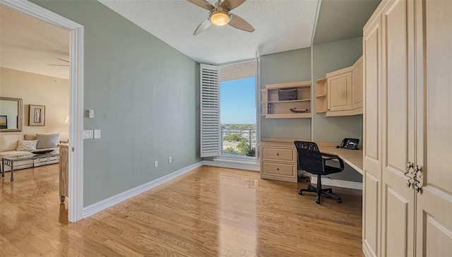 office featuring light wood-type flooring, built in desk, a textured ceiling, and ceiling fan