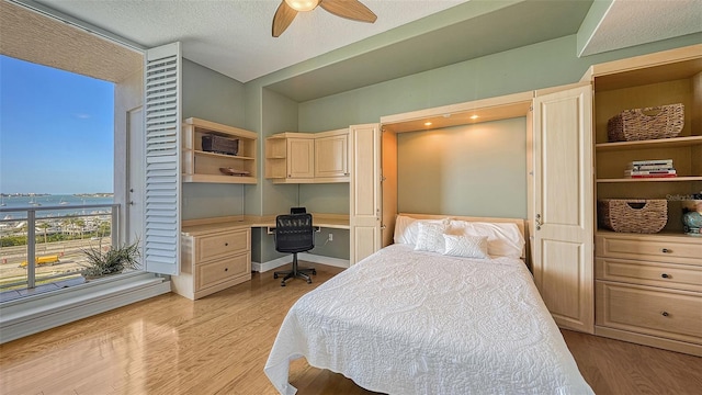 bedroom with ceiling fan, built in desk, light hardwood / wood-style flooring, and a textured ceiling