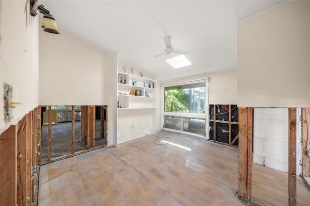 unfurnished living room with ceiling fan, built in features, lofted ceiling with skylight, and wood-type flooring