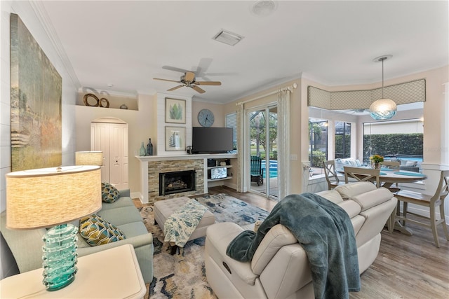 living room featuring ornamental molding, ceiling fan, a fireplace, and light hardwood / wood-style floors