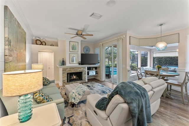 living room with crown molding, light hardwood / wood-style flooring, a stone fireplace, and ceiling fan