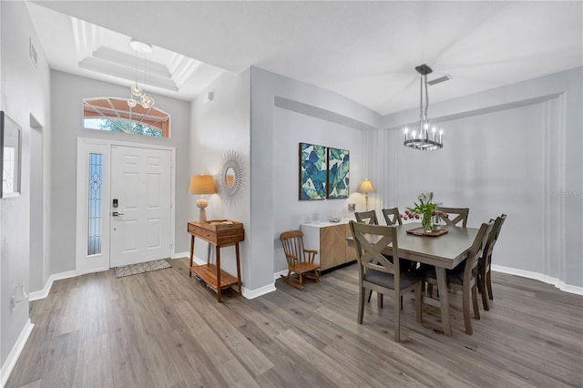 dining area with hardwood / wood-style floors, an inviting chandelier, and a tray ceiling