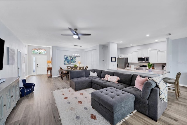 living room with ceiling fan with notable chandelier and light hardwood / wood-style floors