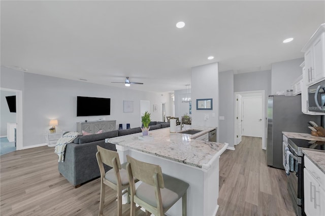 kitchen featuring white cabinetry, a kitchen bar, stainless steel appliances, light stone countertops, and a center island with sink