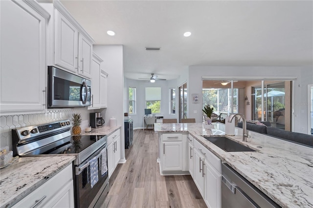 kitchen with sink, appliances with stainless steel finishes, light stone counters, white cabinets, and light wood-type flooring