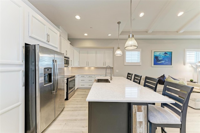 kitchen with sink, white cabinetry, a kitchen island with sink, stainless steel appliances, and decorative light fixtures