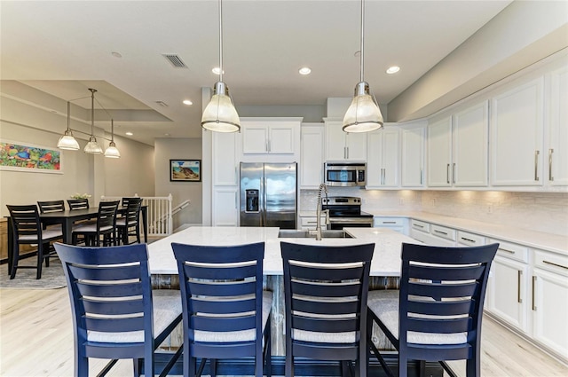 kitchen featuring stainless steel appliances, white cabinetry, a center island with sink, and decorative light fixtures