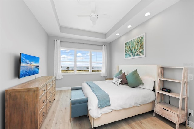 bedroom with ceiling fan, a tray ceiling, and light hardwood / wood-style flooring