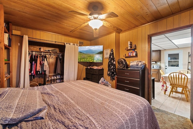 bedroom featuring wood ceiling, wooden walls, a closet, ceiling fan, and light tile patterned floors