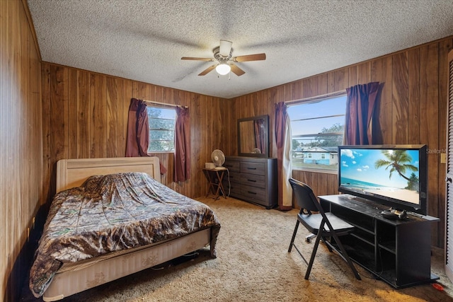 carpeted bedroom with ceiling fan, a textured ceiling, and wood walls