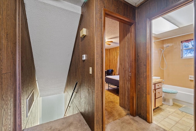 corridor with a textured ceiling, light carpet, and wood walls