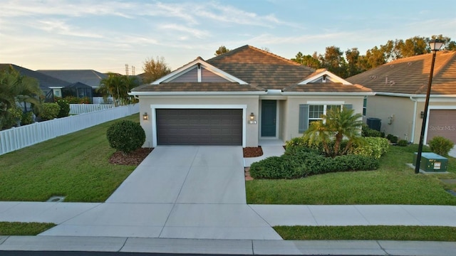 ranch-style house featuring central AC unit, a lawn, and a garage